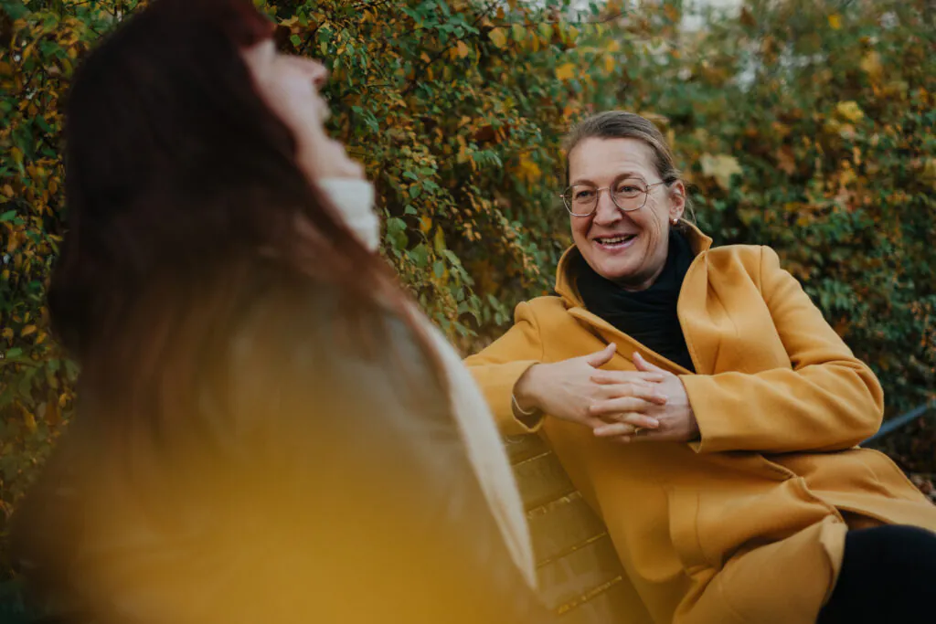 Zwei Frauen unterhalten sich auf einer Bank. Sie lachen.