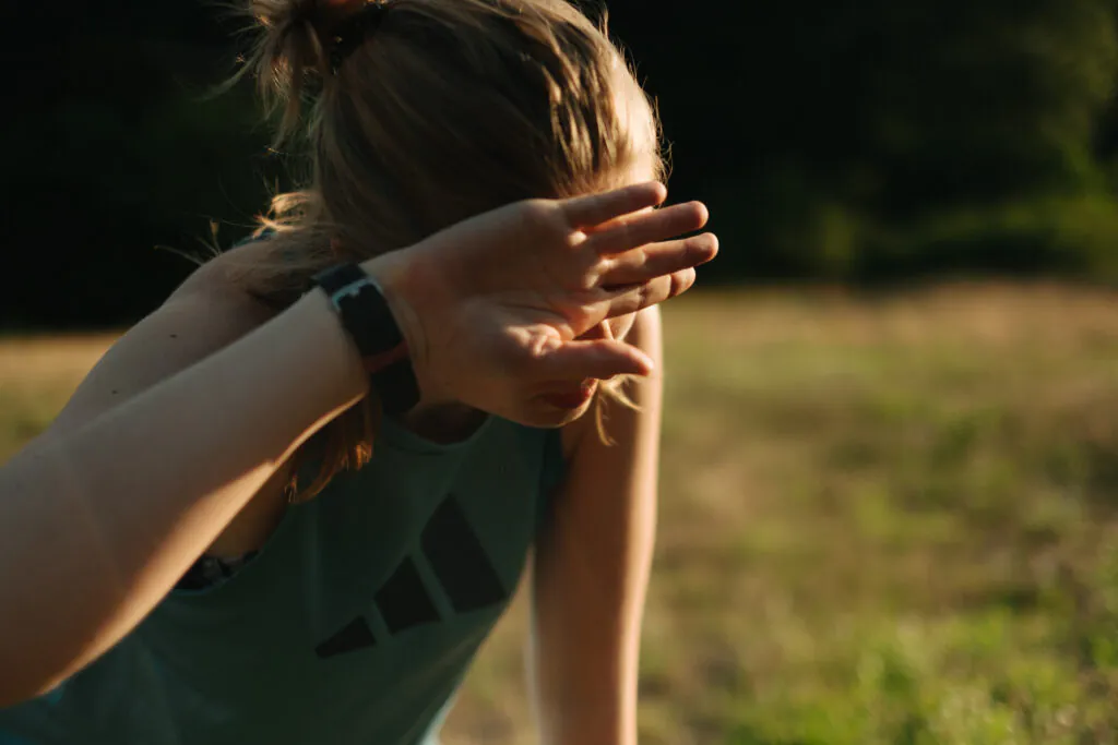 Eine junge Frau ist draußen und hält die Hand vor ihr Gesicht.