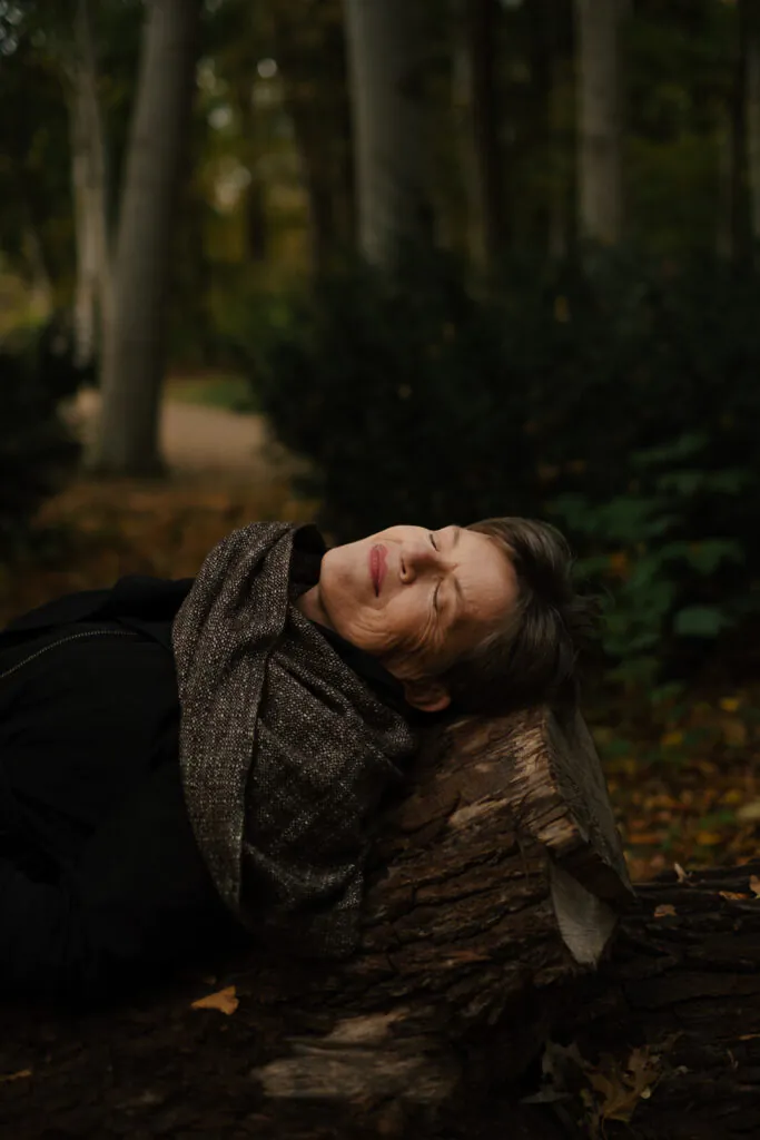 Eine Frau liegt auf einem Baumstamm. Das Licht fällt in ihr Gesicht. Sie hat die Augen geschlossen.