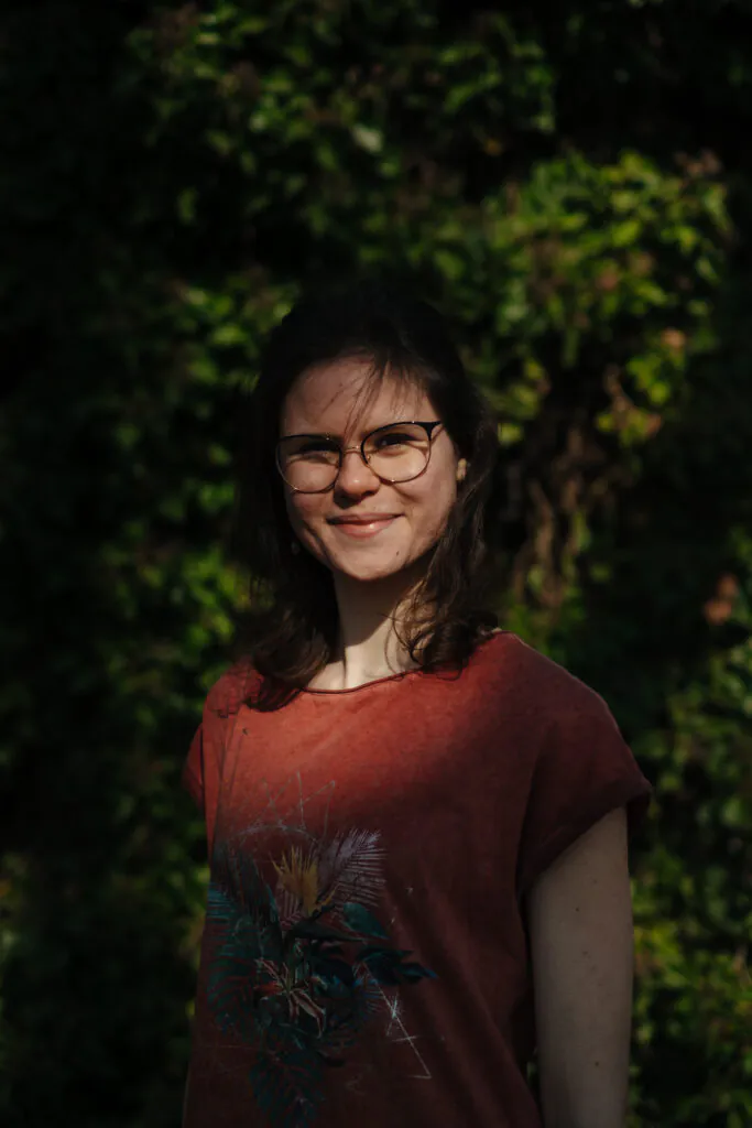 Eine junge Frau steht draußen. Die Sonne scheint in ihr Gesicht.