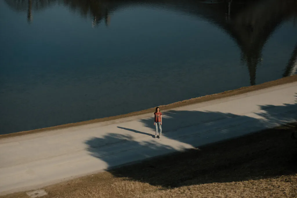 Eine Frau steht auf Rollschuhen auf einer Straße an einem See. Sie ist nur aus der Ferne zu sehen.
