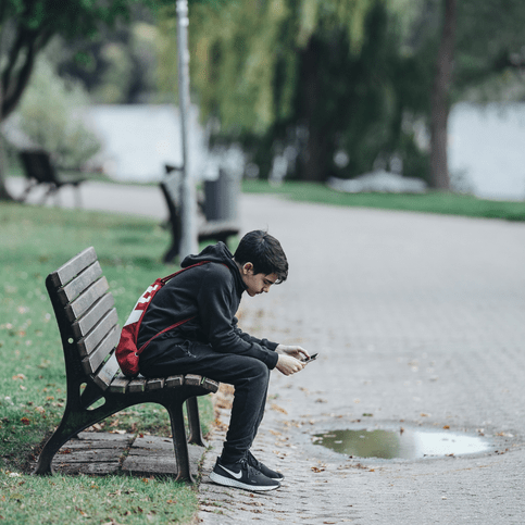 Jugendlicher sitzt mit dem Smartphone in der Hand auf einer Parkbank.