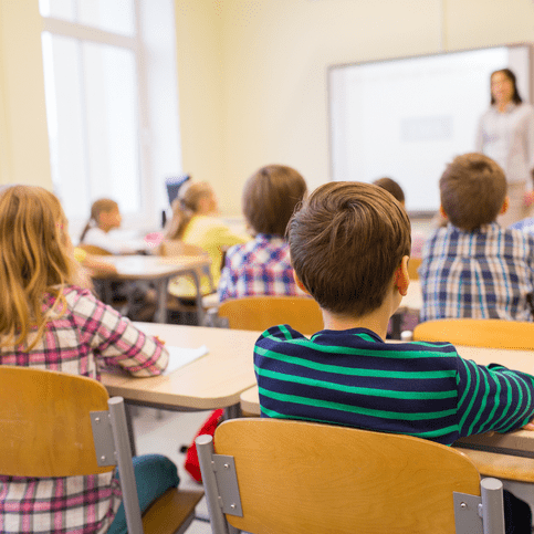 Schülerinnen und Schüler sind in einem Klassenraum. Eine Lehrerin steht vorne.